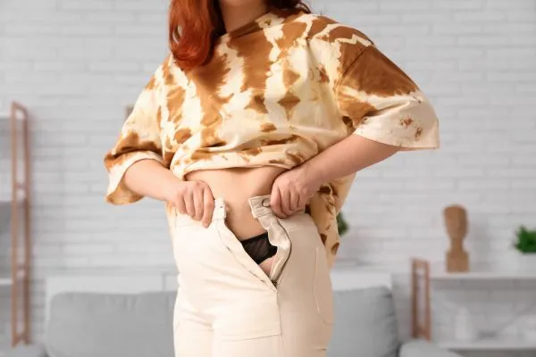 Image of woman trying to do her trousers up after pregnancy weight gain Warminster